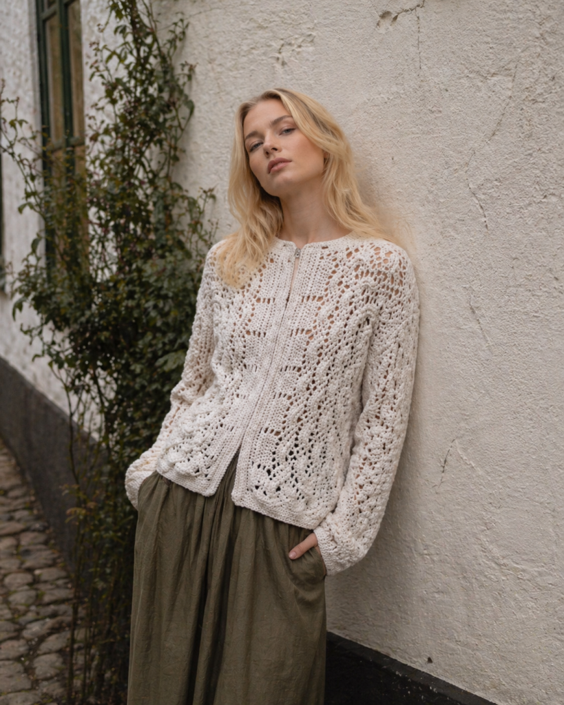 Portrait photo of model wearing white knitted cardigan against rustic wall